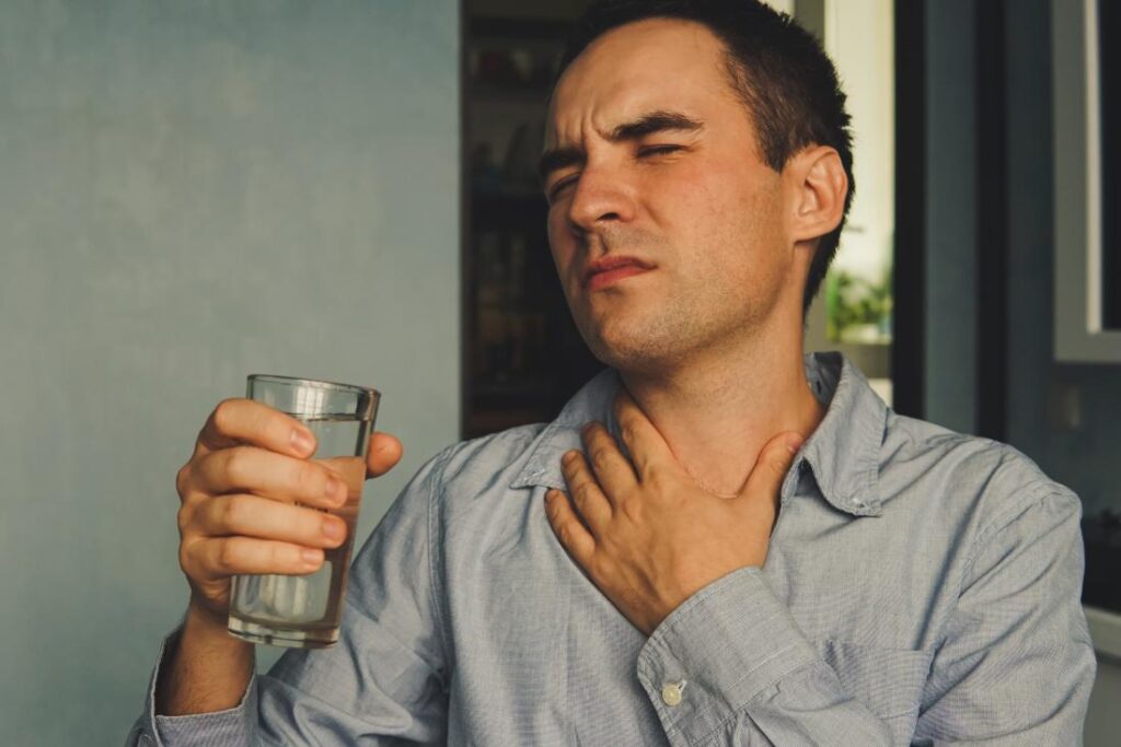 mn-with-dry-throat-clutching-his-neck-in-pain-and-holding-a-glass-of-water